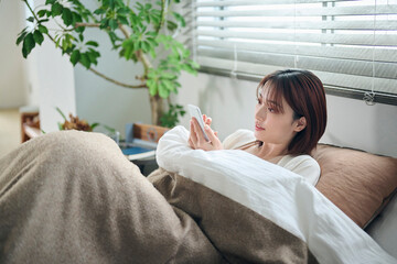 布団に入ってスマートフォンを見る20代女性