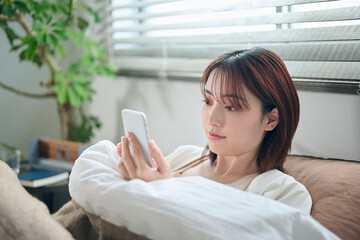 布団に入ってスマートフォンを見る20代女性