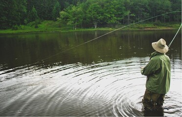 Man standing in a lake with waders on,  fly fishing. 