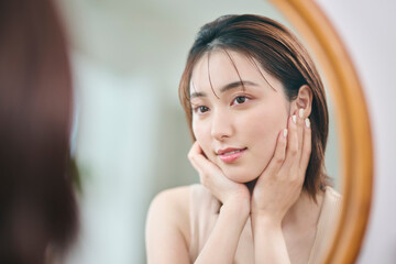 Naklejka premium 自分の肌に触れる20代女性,反射,鏡