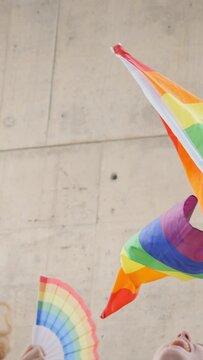 Vertical. LGBT rainbow waving in wind in front of a wall. Hand holding gay pride flag. Diverse people dancing and enjoy under flag. Lesbian, gay, bisexual, homosexual, transgender social movements