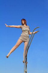 Eine junge Frau im Kleid steht hoch oben auf einer Leiter und streckt einen Arm und ein Bein aus
