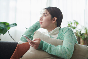 ソファでくつろぎながらスマートフォンを見る女性