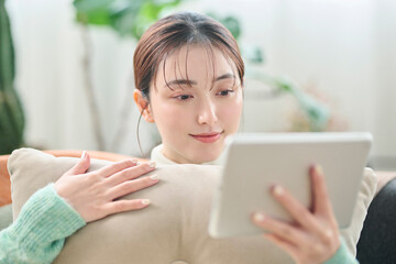 ソファでくつろぎながらタブレット端末を見る女性