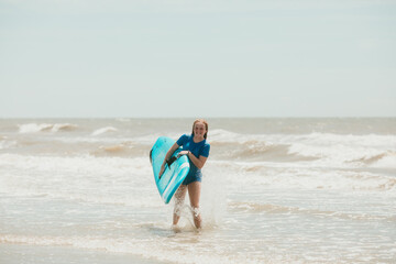 Teen girl holding a surf board leaving the ocean with rash guard shirt on.