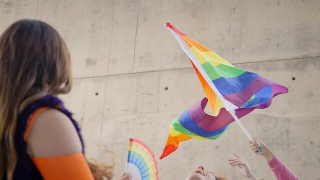 LGBT rainbow waving in wind in front of a wall. Hand holding gay pride flag. Diverse people dancing and enjoy under flag. Lesbian, gay, bisexual, homosexual, transgender social movements