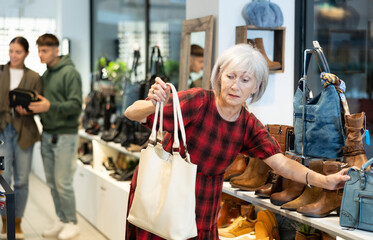 Elderly woman in casual clothes chooses handbag in store.. - Powered by Adobe