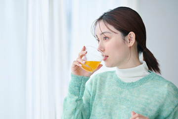 窓際でオレンジジュースを飲む20代女性