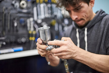 Hispanic worker preparing a spray paint gun in his bike workshop to airbrush a bicycle.