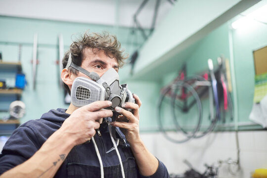 Portrait of a latin young worker putting on a protective respirator mask in his workshop. Real people at work. - Powered by Adobe