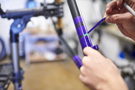 Unknown person working on a custom bike frame painting design in purple and black, a creative and technical handcrafted process. Time to remove the masking tape lines. Close up view of the hands.