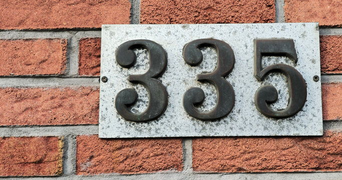 Number plate. Number 335 against a red brick wall background. Concept from a room and a wall. High resolution 150 megapixels