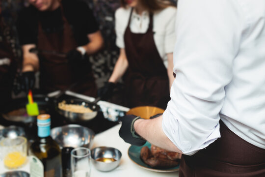 Group of guests in a cooking class studio, adults preparing different dishes in the kitchen together, people in aprons learn on culinary master class, chef uniform, hands in gloves, italian cuisine