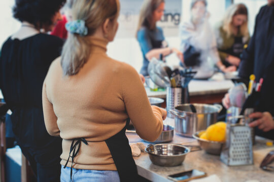 Group of people in a cooking class studio, adults preparing different dishes in the kitchen together, people in aprons learn on culinary master class, chef uniform, hands in gloves, italian cuisine