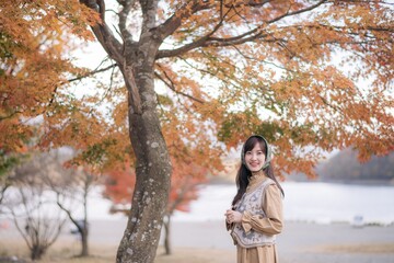 Asian woman in casual dress enjoys Japan's beauty, walking amid vibrant foliage. A cheerful holiday portrait capturing the essence of nature, fashion, and a journey.