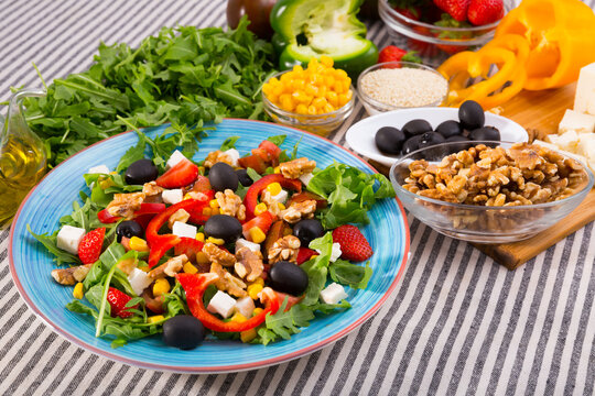 Salad with arugula, olives, Feta cheese, corn and walnut and its ingredients in the kitchen.