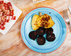 Fried morcilla (blood sausage with rice) served with side dish of baked potatoes