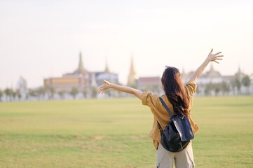 A Traveler Asian woman in 30s, bathed in golden glow of a Bangkok sunset, laughs with carefree joy, her arms outstretched as if to embrace freedom of the moment. Backpack strapped on.