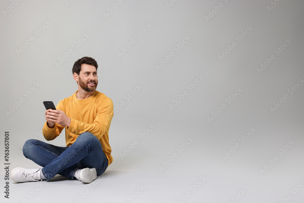 Poster smiling man with smartphone on grey background. space for text