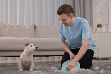 Smiling man with brush and pan removing pet hair from carpet at home