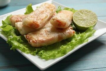 Delicious fried spring rolls on light blue wooden table, closeup