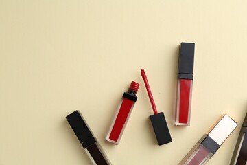 Different lip glosses and applicator on pale yellow background, flat lay. Space for text