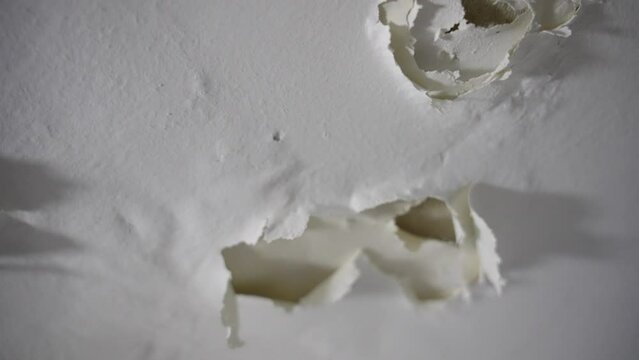 Peeling dry paint falling off wall or ceiling in bathroom or shower room in house or apartment. Close up - cracks of white paint falling apart in neglected place with moisture or humidity condensation