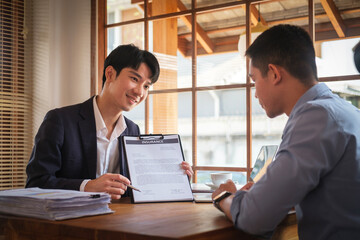 Male insurance agent showing place for signature on paper contract document to client.