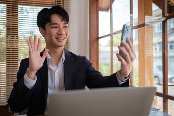 Happy young businessman holding mobile phone and making call at his office.