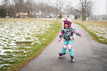 Happy Asian girl kid wearing snow suit and safety guard helmet having fun while playing rollerblade...