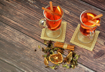 Two glasses of hot red wine with citrus pieces, cinnamon and spices on a wooden table.