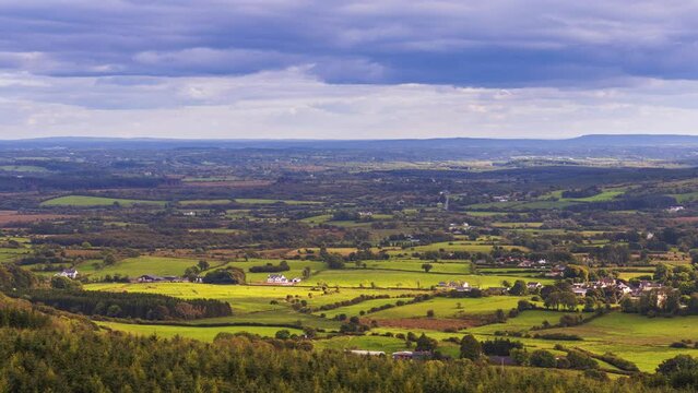 Time lapse of rural farming landscape of local farmhouses with forest and hills during a cloudy day viewed from above Lough Meelagh in county Roscommon in Ireland.