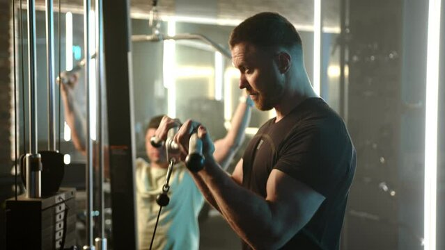 Two sportsmen are immersed in a dedicated workout on the cable crossover machine, syncing their routines in a well-lit, high-energy gym setting. Camera 8K RAW. 
