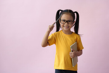 A cute girl wearing glasses holds a pen and writes ideas in a notebook, writes ideas in a planner, and holds a notebook diary. A child with a brilliant idea of time management learning education.