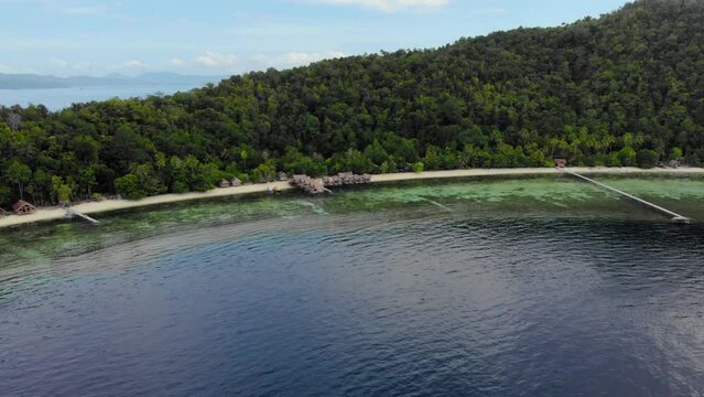 Island landscape with sandy beach and guesthouses, lush greenery, clear water. Aerial tilted shot.