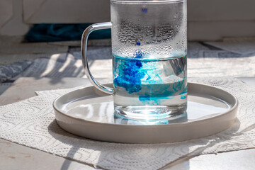 Glass mug with hot water, into which blue food coloring is dripped. Preparation for coloring Easter...