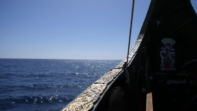 A viking ship longboat with ornate Nordic carvings on ship's bow with a rope, sparkling ocean backdrop. A vintage sea pirate nautical theme captured on a bright, sunny day