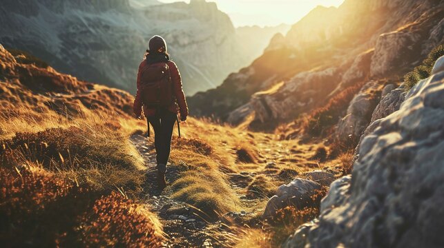 The image captures a solitary hiker from behind, walking through a rugged mountainous terrain at either dawn or dusk. The hiker is dressed in warm outdoor clothing and a backpack, suggesting preparedn