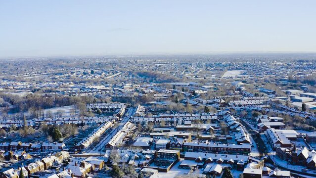 Clear bright and sunny snow day in Birmingham, United Kingdom. Drone moves foward and downward, high above residential homes and streets. The city looks dense and vast.