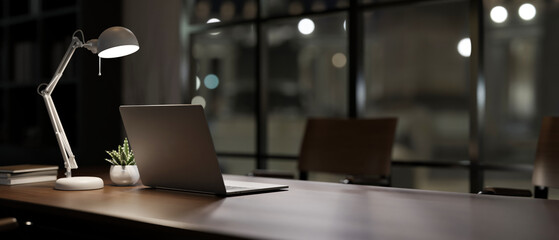 A back view image of a laptop computer on a meeting table in a modern dark meeting room.