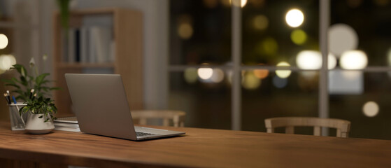 A back view image of a laptop on a dining table in a comfortable, minimalist dining room at night.