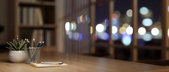 A hardwood desk with stationery and a potted plant in a contemporary home office at night.