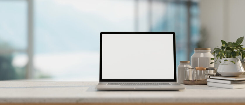 A close-up image of a laptop computer mockup and accessories on a table in a modern room.