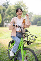 Obraz premium A cheerful and smiling young Asian woman is riding her bike in the green park on a sunny day.