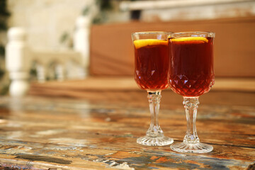Two Glasses of Iced Tea on a Vintage Table. Two crystal glasses filled with a dark amber liquid and garnished with orange slices sit on a rustic wooden table.
