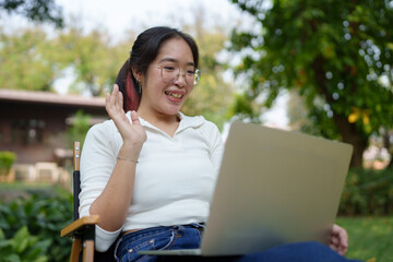 Young women wearing glasses wearing headphones reading a book Making diary notes Video calls via laptop online, relaxing, lifestyle, vacation, at the park Happily natural place.