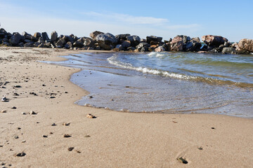 Fototapeta na wymiar Sandy shore with water against a backdrop of large rocks. Beautiful photo wallpaper of nature.