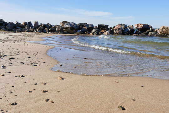 Sandy shore with water against a backdrop of large rocks. Beautiful photo wallpaper of nature.