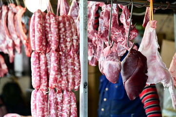 In a market stall, a pork vendor showcases hanging pork liver and heart, alongside strings of sausages, with various other meat products in the background.