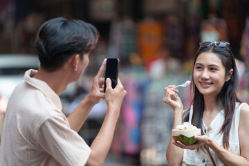 Cute and happy Asian tourist couple holding hands Take photos to keep as souvenirs of delicious food and fruit. While visiting Chiang Mai Old City Market together.